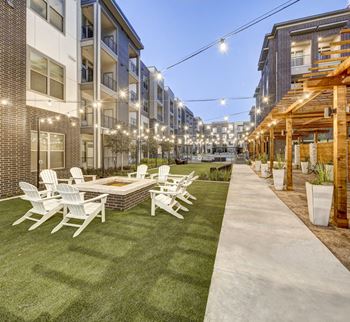 A patio with white chairs and a table is surrounded by apartment buildings.